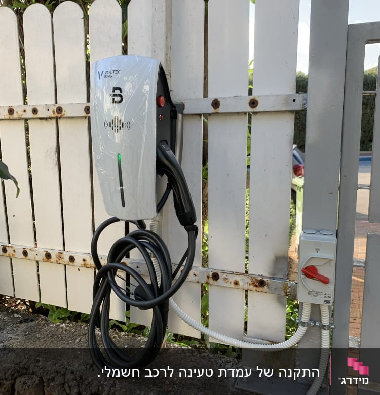 מטען לרכב חשמלי מותקן על גדר עץ לבנה